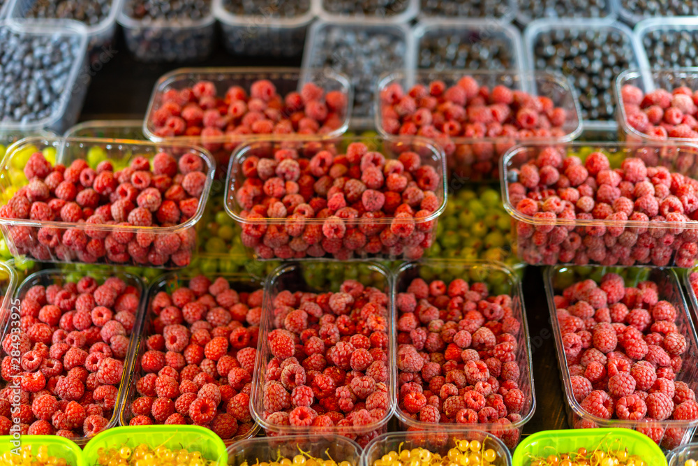 Bright juicy red raspberries in a plastic container on a store counter.