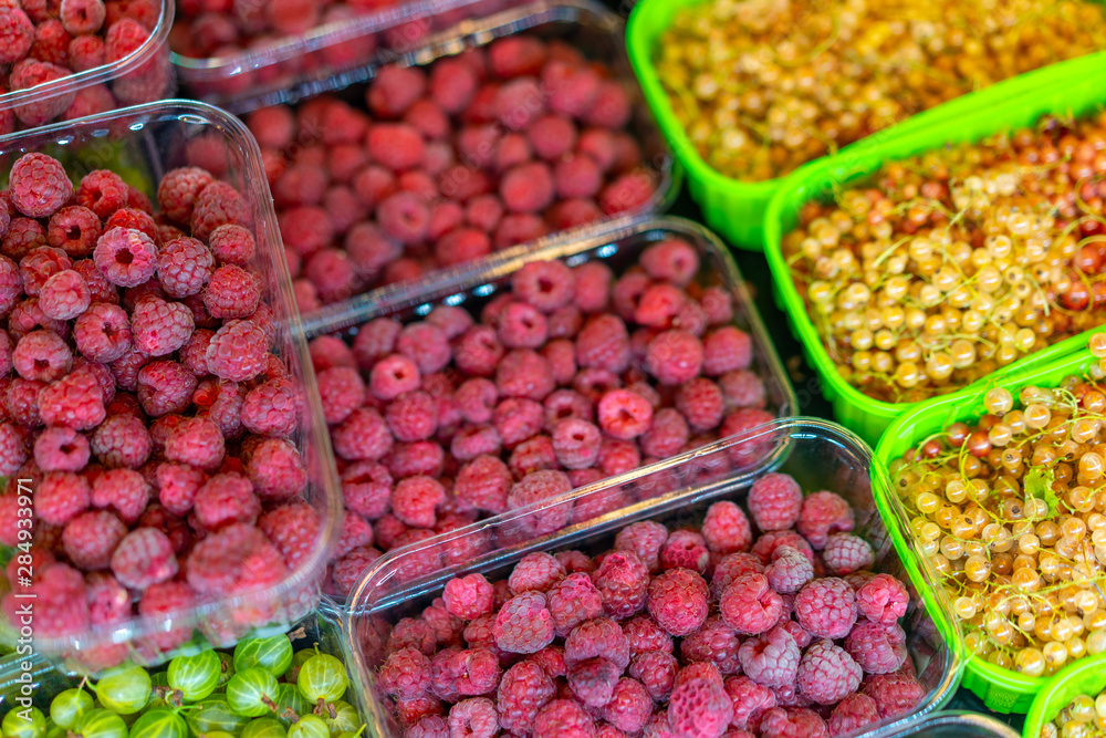 Bright juicy red raspberries in a plastic container on a store counter.