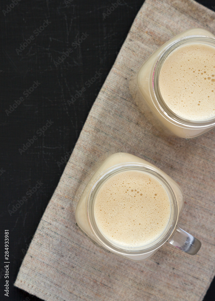 Peanut butter banana smoothie in glass jar mugs on a black surface, overhead view. Flat lay, from above, top view. Copy space. Peanut butter banana smoothie in glass jar mugs on a black surface, overhead view. Flat lay, from above, top view. Copy space.