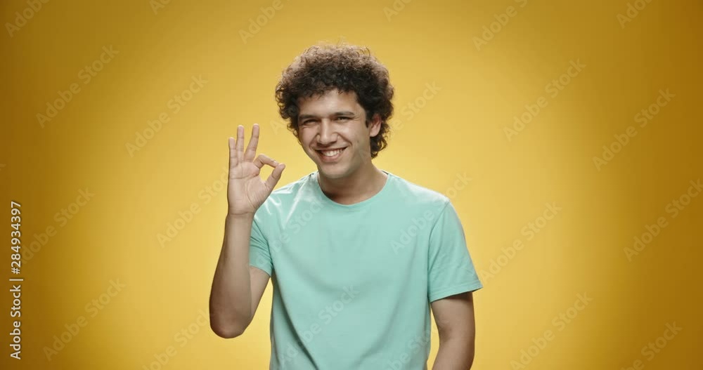 Asian guy with curly hair in casual clothes looking at camera, cheerfully smiling and gesturing ok, isolated on yellow background - close up shot 4k Asian guy with curly hair in casual clothes looking at camera, cheerfully smiling and gesturing ok, isolated on yellow background - close up shot 4k