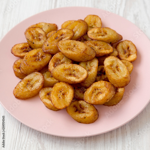 Homemade fried plantains on a pink plate on a white wooden background, side view. Close-up.