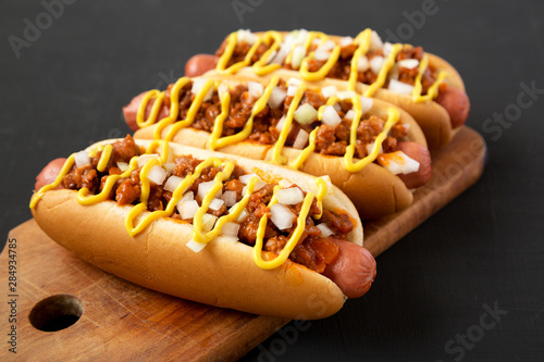 Homemade Detroit style chili dog on a rustic wooden board on a black background, low angle view. Close-up.
