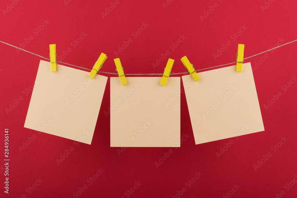 yellow notebook paper sheets for notes and reminders, fastened with decorative yellow clothespins hanging on a rope on a red background yellow notebook paper sheets for notes and reminders, fastened with decorative yellow clothespins hanging on a rope on a red background