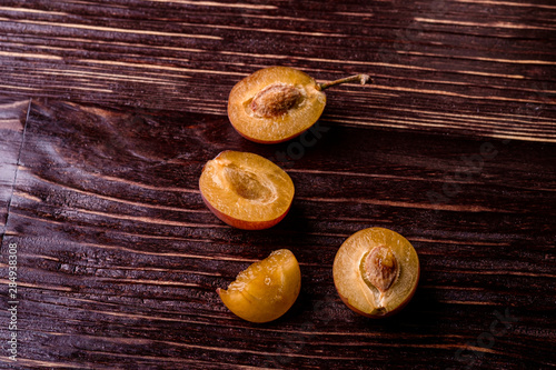 Scattered sliced half ripe sweet plum fruits with water drops on dark moody wood table background, macro, close up