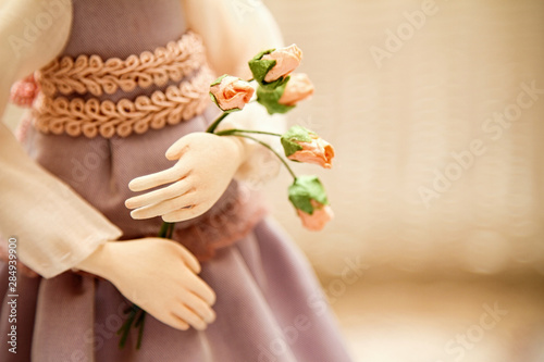 Photo in delicate pastel colors. Doll's hands holding a bouquet with roses with blurred background