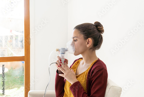 Young woman doing inhalation nebulizer in hospital, holding a mask nebuliser inhaling asthma and bronchitis medication to improve breathing. Healthcare, medicine, disease concept.