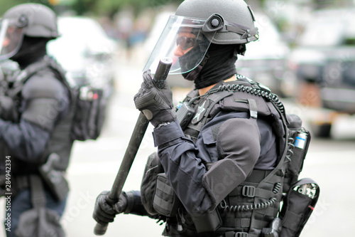 Police officer in riot gear overseeing a crowd of protestors.