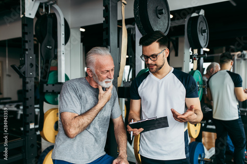 Senior man exercising in gym with his personal trainer. Fototapeta