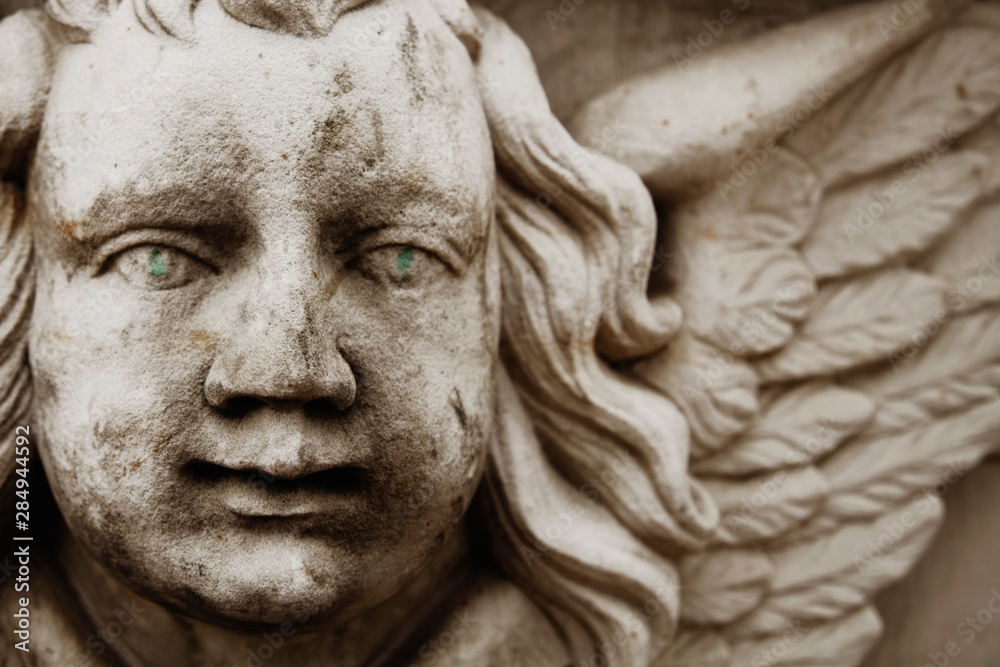 Fragment of ancient statue of angel with wings and green eyes