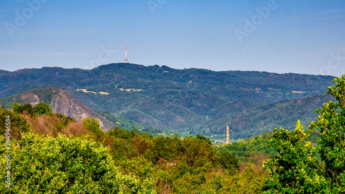 A mountainous landscape with a chimney in the valley and a television transmitter on top of a hill - Bukova Hora TV Tower photo