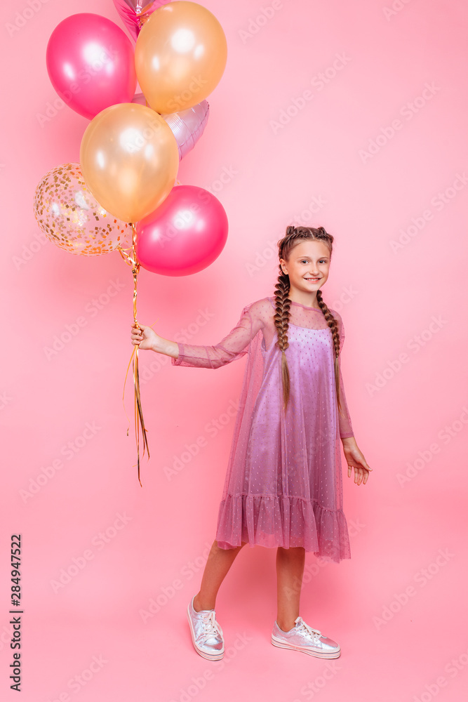 Happy and beautiful teen girl holding a bunch of colorful balloons and looking at camera with smile on pink background Happy and beautiful teen girl holding a bunch of colorful balloons and looking at camera with smile on pink background