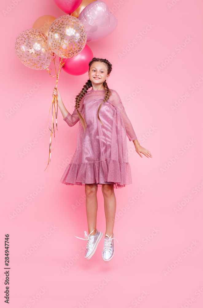 Happy teenage girl jumping high with balloons isolated on pink background Happy teenage girl jumping high with balloons isolated on pink background