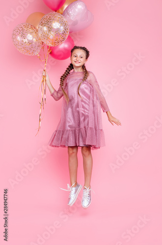 Happy teenage girl jumping high with balloons isolated on pink background