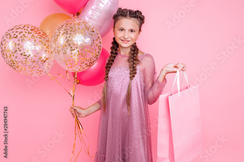 Happy girl with balloons and shopping bags posing on a pink background