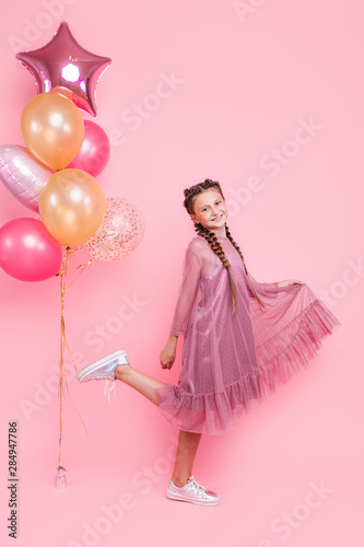 Happy and beautiful teen girl holding a bunch of colorful balloons and looking at camera with smile on pink background