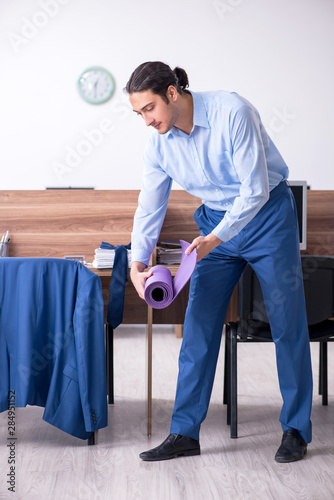 Young handsome businessman doing exercises at workplace