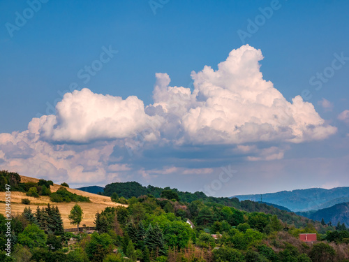 Rain clouds - Cumulonimbus - forming in the blue sky over hilly landscape