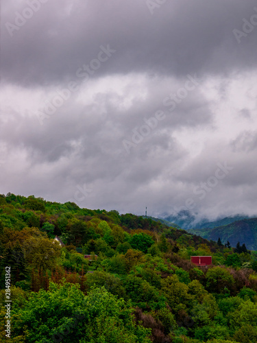 Heavy rain clouds cover the tops of wooded hills
