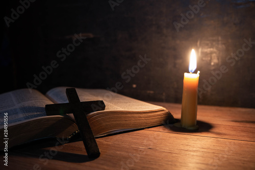 Cross with bible and candle on a old oak wooden table.