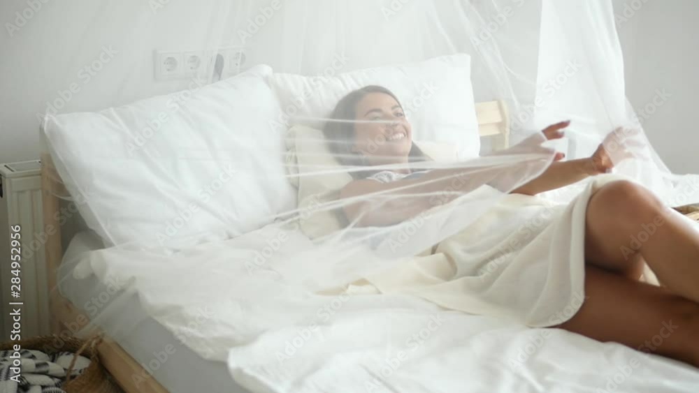 A beautiful girl slowly wakes up in the morning, stretches herself in bed and smiles, the sun shines on her from a large window. Happy young girl meets a new day A beautiful girl slowly wakes up in the morning, stretches herself in bed and smiles, the sun shines on her from a large window. Happy young girl meets a new day