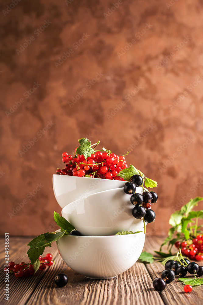 Fresh ripe red black currant berry in white bowls stand in a pile on the table. Selective focus. Vertical frame
