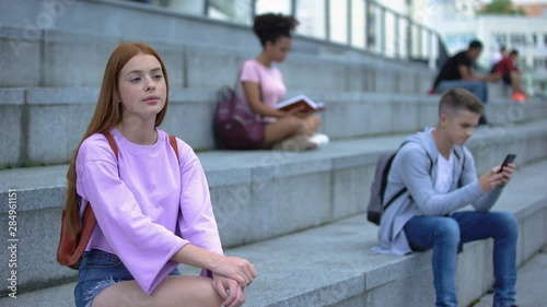 Sad female student sitting alone campus stairs, unsociable teenager problems