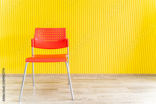 Red plastic chair on a wooden floor with a yellow background.