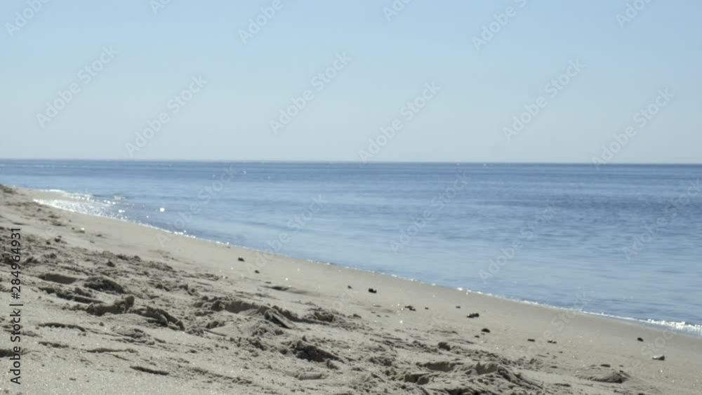 Zoom in on glittering waves hitting a beach shoreline with footprints in the sand on a warm and quiet sunny day Zoom in on glittering waves hitting a beach shoreline with footprints in the sand on a warm and quiet sunny day