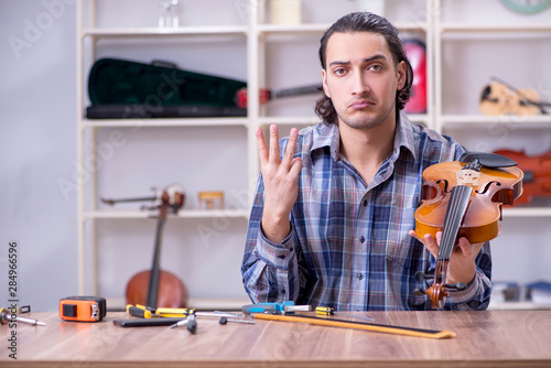 Young handsome repairman repairing violin