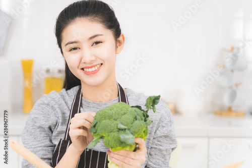 Beautiful asian woman is preparing to cook healthy food which consists of a variety of fruits and vegetables for the family. Portrait of housewife is smiling and holding broccoli.