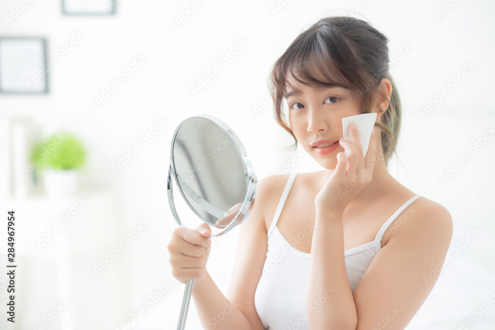 Beautiful young asian woman smile and joy with skin care use oil blotting paper on face looking mirror in the room, beauty asia girl happy and cheer makeup and cosmetic, health care on facial concept. Beautiful young asian woman smile and joy with skin care use oil blotting paper on face looking mirror in the room, beauty asia girl happy and cheer makeup and cosmetic, health care on facial concept.