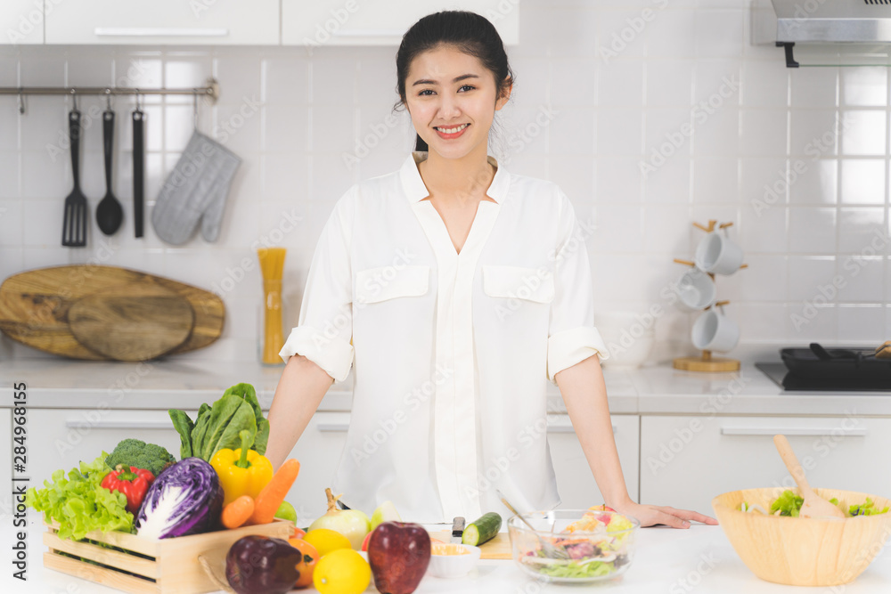 Portrait of beautiful asian woman is sitting in the bright white kitchen. wife or housewife is preparing to cook healthy food which consists of a variety of fruits and vegetables for the family. Portrait of beautiful asian woman is sitting in the bright white kitchen. wife or housewife is preparing to cook healthy food which consists of a variety of fruits and vegetables for the family.