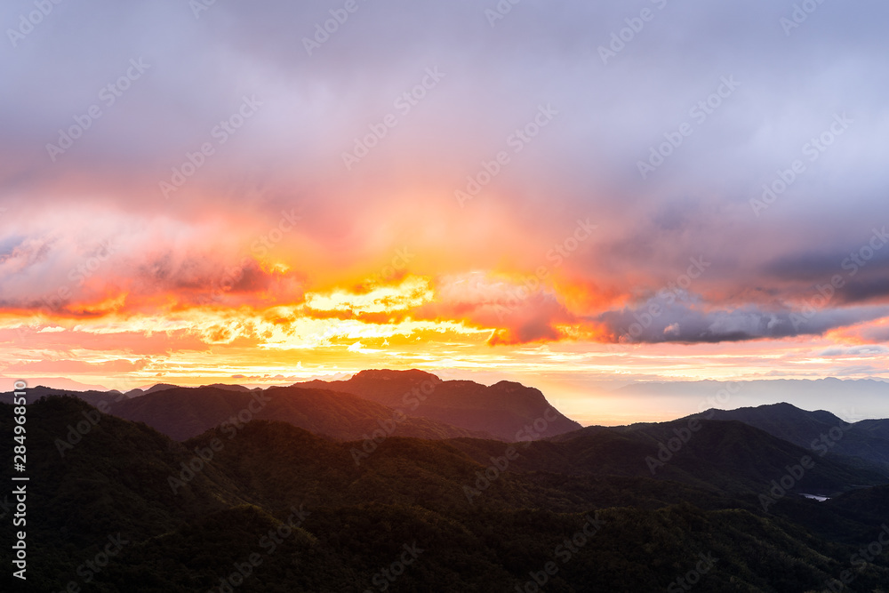 Landscape of mountains layered with cloudy sky and sunrise.