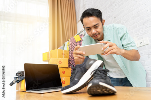 фотографія Asian man working taking photo to shoes with smart phone for post to sell online