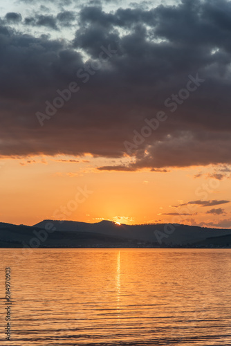 Burning red sunset on the river. Men riding boat. Silhouette of mountains on the background. Beautiful clouds in the sky.