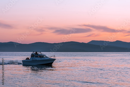 Sunset on the river. Men riding boat. Silhouette of blue mountains on the background. Beautiful pink clouds in the sky.