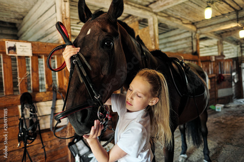 A teenage girl rider saddles a horse and puts a bridle on her.