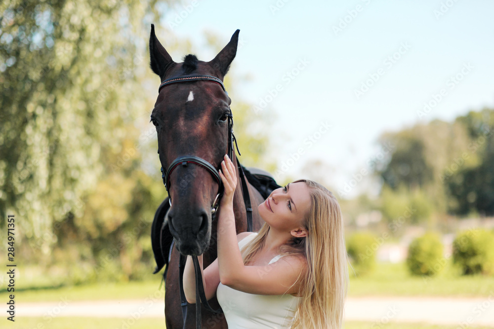 Fototapeta premium Young attractive blond woman hugs a brown horse.
