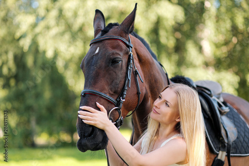 Young attractive blond woman hugs a brown horse. © spaskov