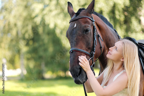 Young attractive blond woman hugs a brown horse.