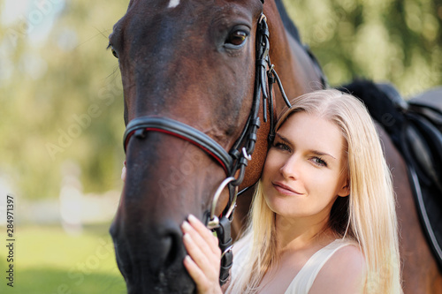 Young attractive blond woman hugs a brown horse. © spaskov
