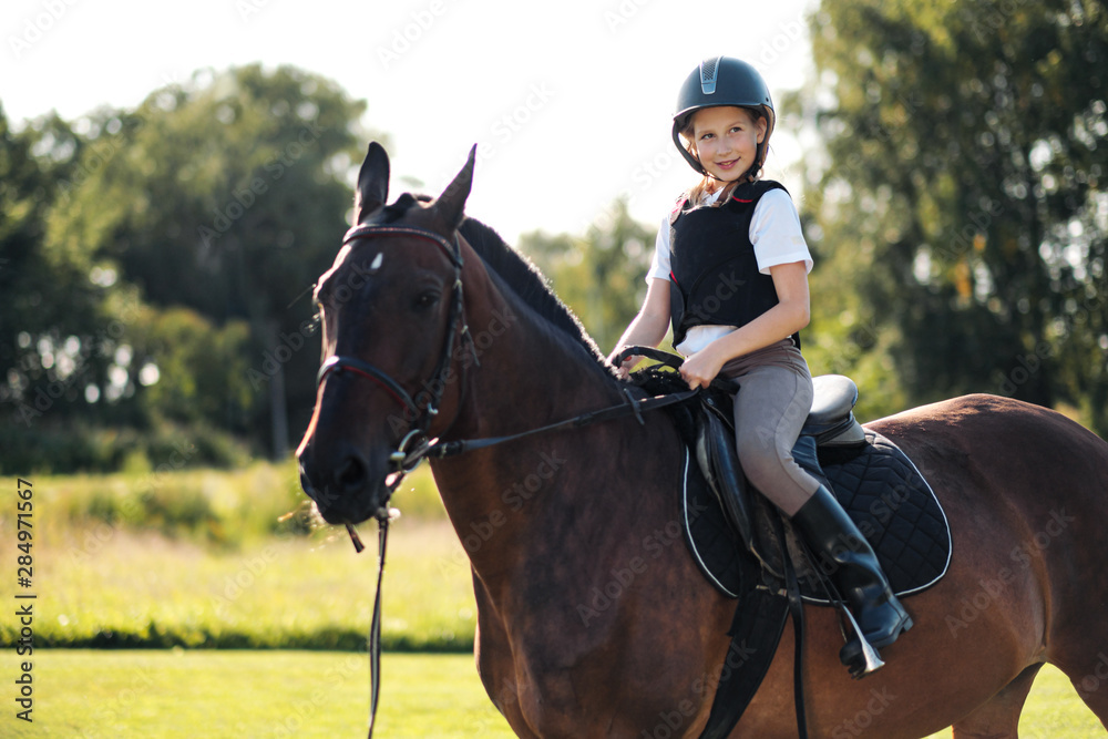 Girl teenager jockey sits on a brown horse in nature. Girl teenager jockey sits on a brown horse in nature.