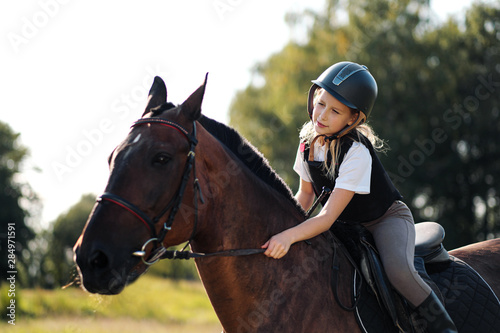 Girl teenager jockey sits on a brown horse, hugs and strokes her.