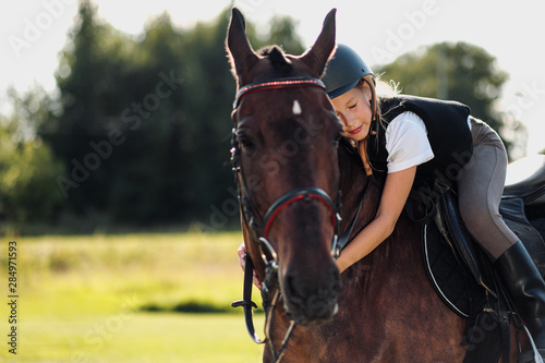 Girl teenager jockey sits on a brown horse, hugs and strokes her.