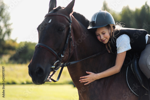 Girl teenager jockey sits on a brown horse, hugs and strokes her. © spaskov