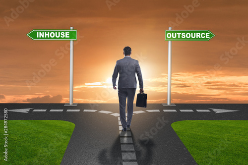 Businessman at crossroads deciding between outsourcing and inhou