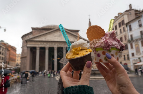 Two glasses of Italian ice cream in the hands of a girl against the Roman Pantheon in Piazza della Rotonda in Italy on a rainy day photo