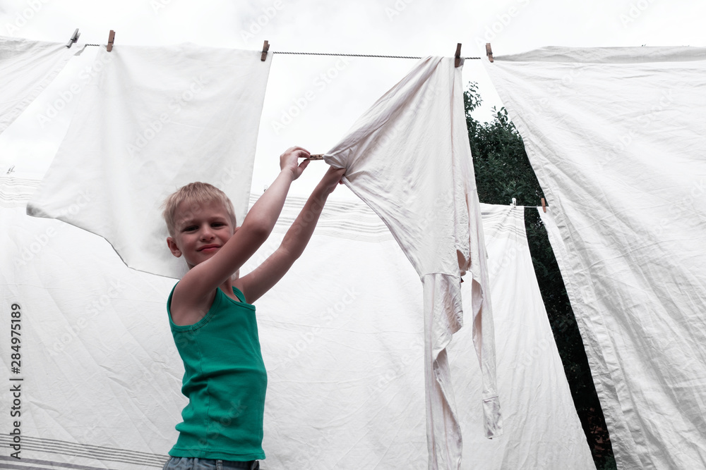 Blond boy helps mom hang clean clothes in the yard with a clothespin