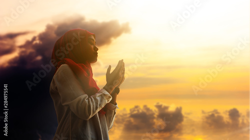 Silhoueitte of young muslim woman pray with beautiful sunset/ sunrise in background photo