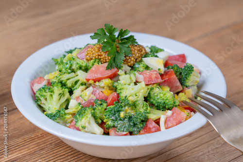 Delicious salad with broccoli, tomato, onion and boiled egg with cream sauce in plate on wooden background. Healthy food